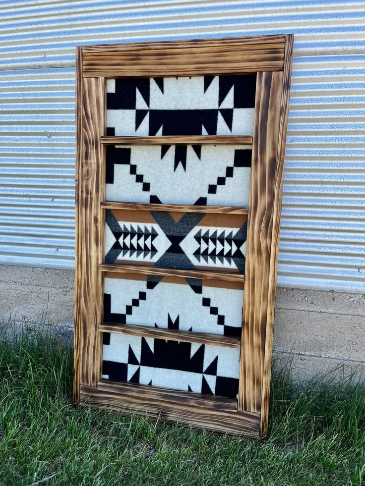 a wooden frame sitting on top of grass next to a metal building with a black and white pattern