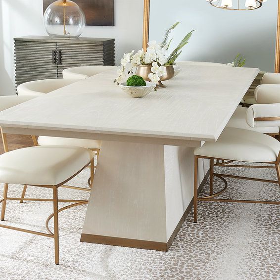 a dining room table with white chairs and flowers on the centerpiece, in front of a mirror