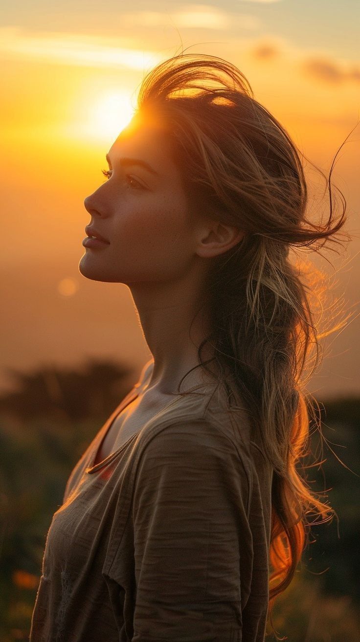 a woman standing in front of the sun with her long hair blowing in the wind