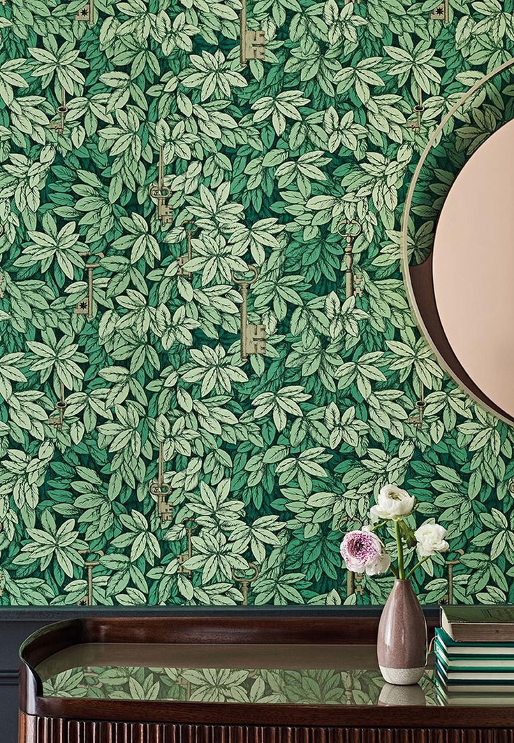 a mirror and vase with flowers on a table in front of a green wallpaper