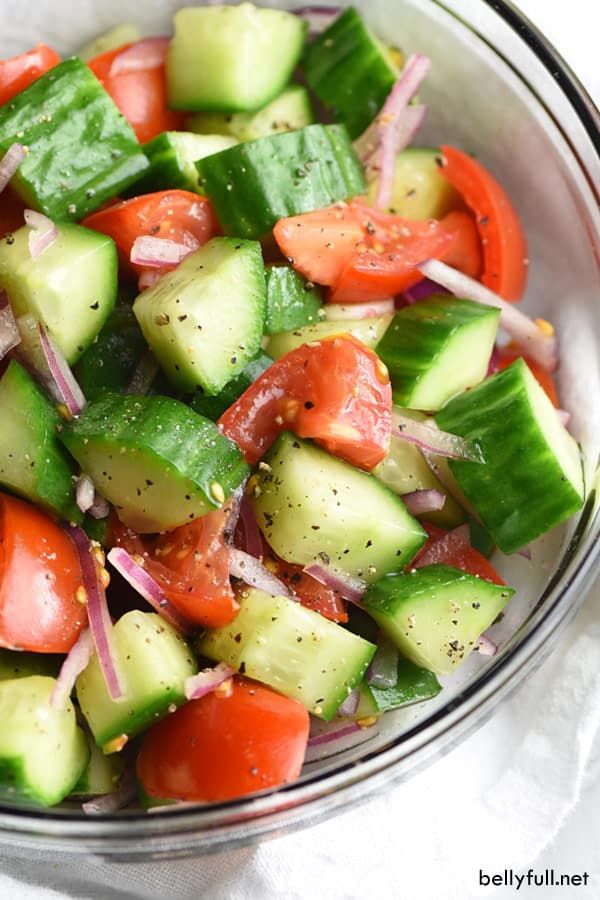 a glass bowl filled with cucumber, tomatoes and onion salad on top of a white cloth