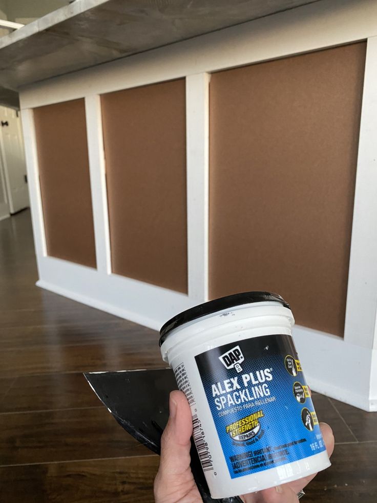 a person holding a bucket of paint in their left hand while standing on a hard wood floor