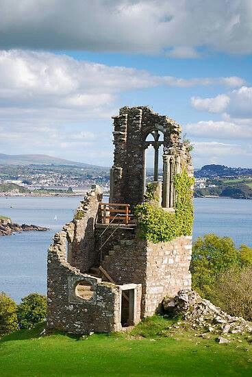 an old stone building sitting on top of a lush green hillside next to the ocean