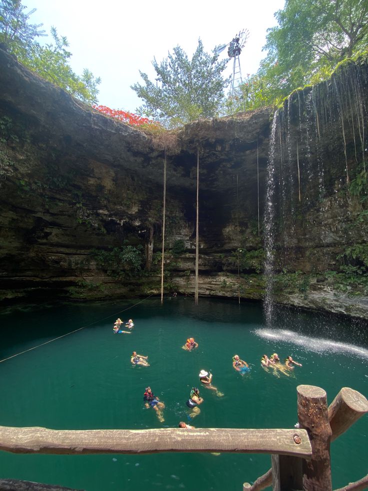 people are swimming in the water near a waterfall with a rope hanging from it's side