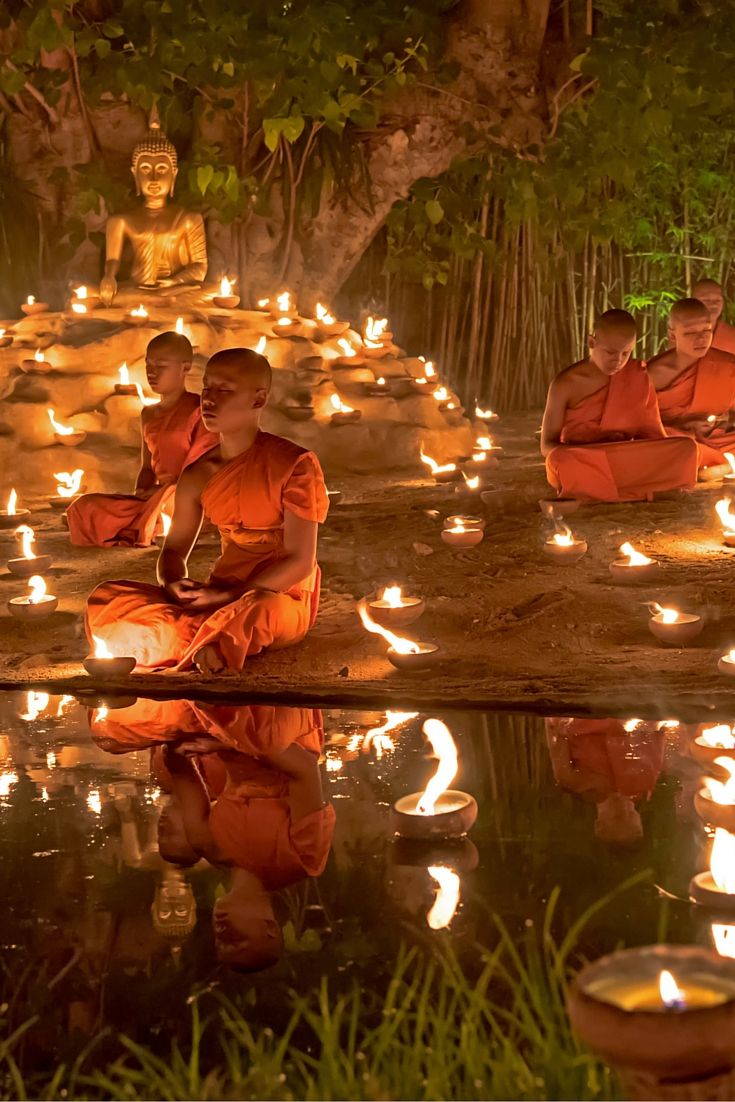 buddhist monks sitting on the ground with candles in their hands