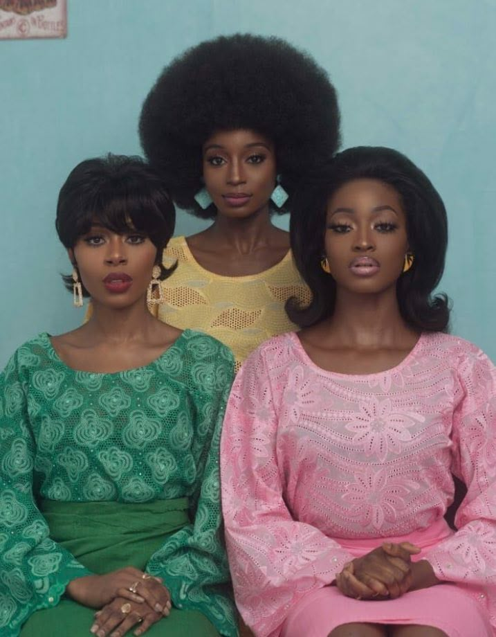 three women sitting next to each other in front of a blue wall with an afro hairstyle