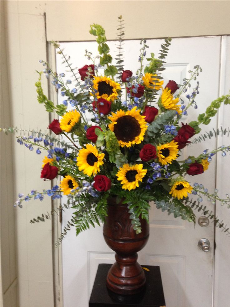 a vase filled with sunflowers and other flowers on a black stand in front of a door