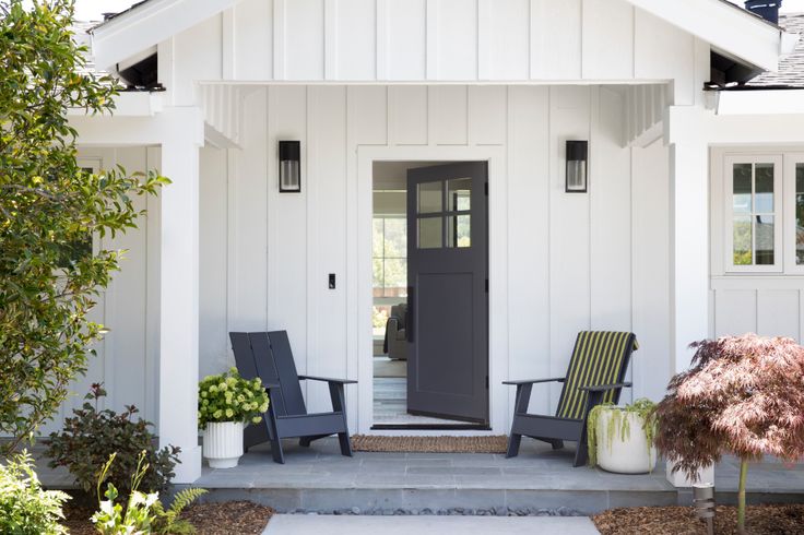 two chairs are sitting in front of a white house with black door and window frames