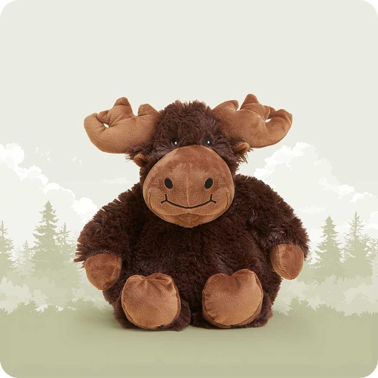 a brown stuffed moose sitting on top of a green field with trees in the background