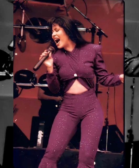 a woman singing into a microphone while wearing red pants and a cropped top with sequins on it