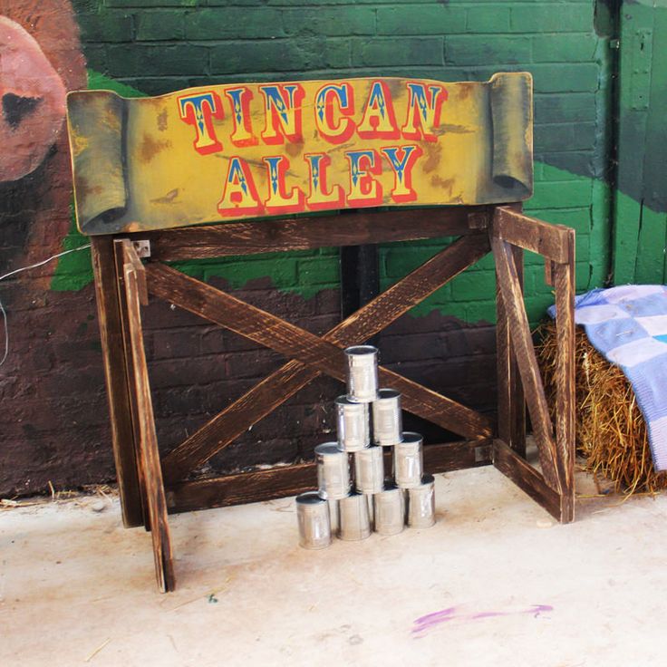 a sign that says tin can alley next to hay bales on the ground in front of a brick wall