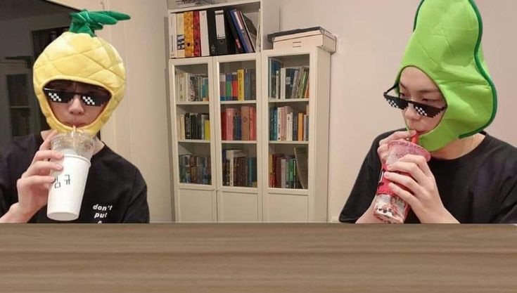 two people wearing pineapple hats and holding drinks in front of their faces while sitting at a table