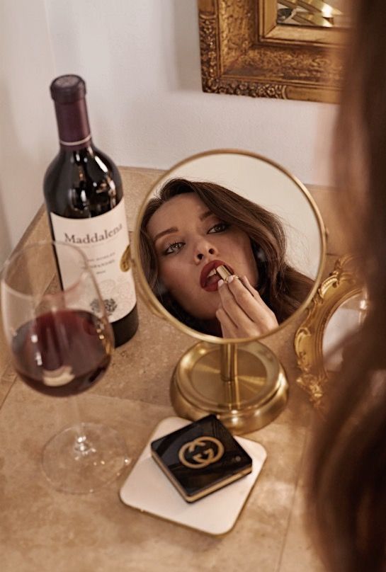 a woman brushing her teeth in front of a mirror with a bottle of wine next to it