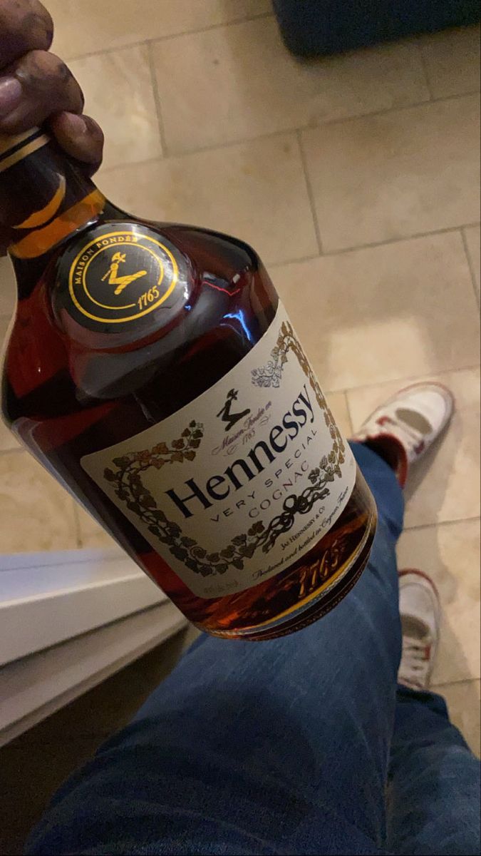 a bottle of hennesy is being held by someone's feet on the floor