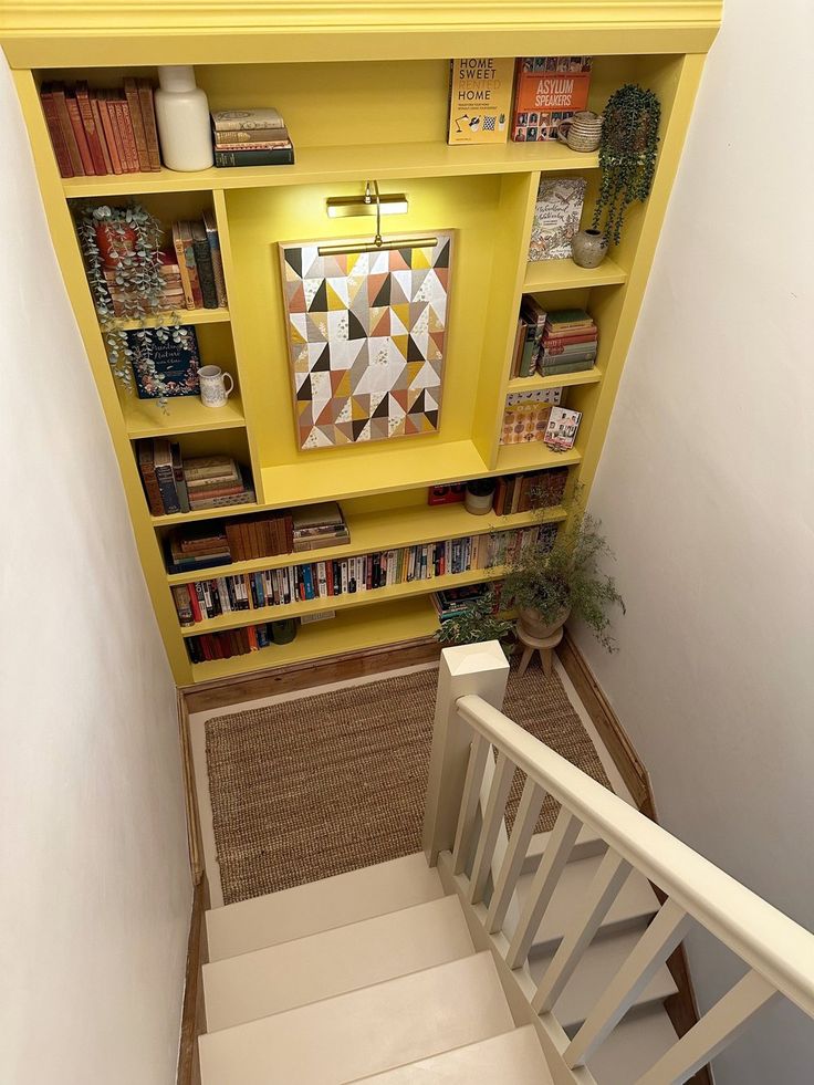 stairs leading up to a bookshelf with yellow shelves on each side and white handrails