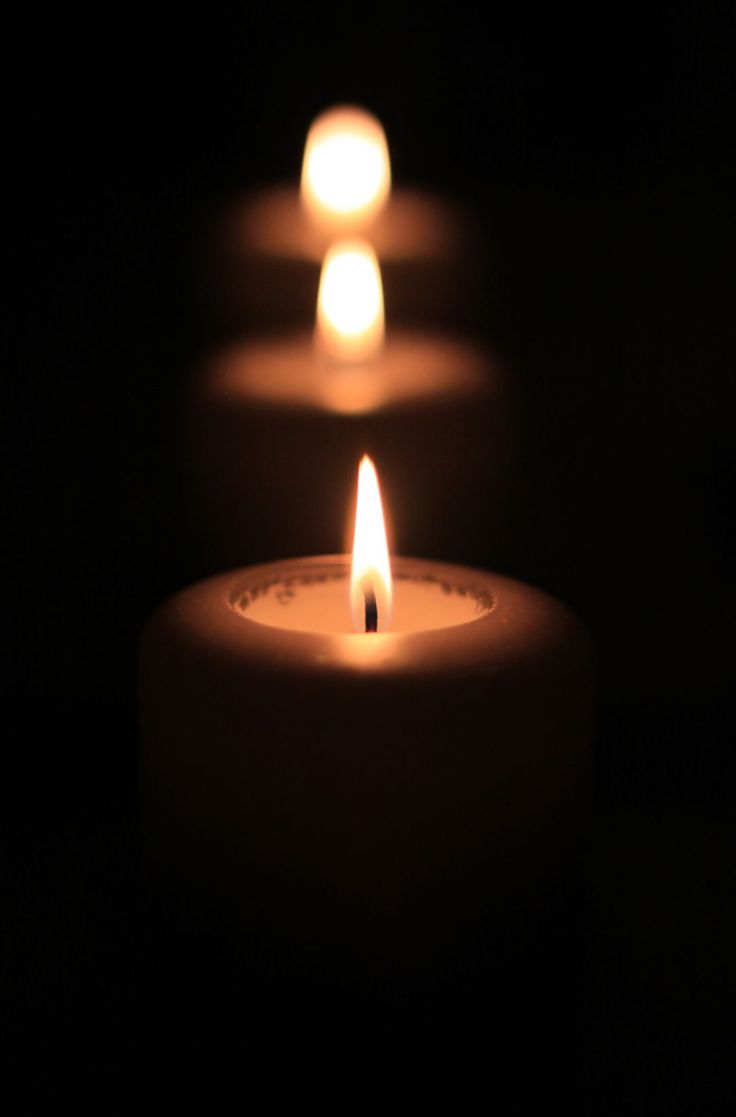 three lit candles in the dark with one glowing