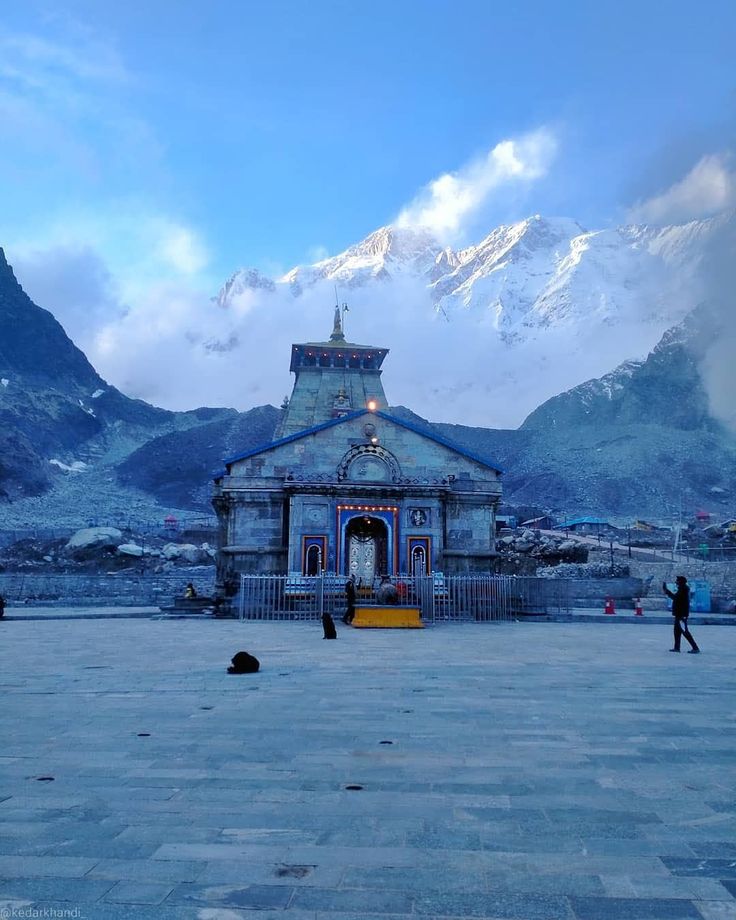 people are walking around in front of a building with mountains in the backgroud