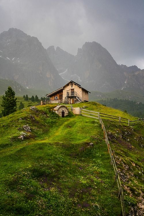 a house sitting on top of a lush green hillside covered in grass and mountains behind it