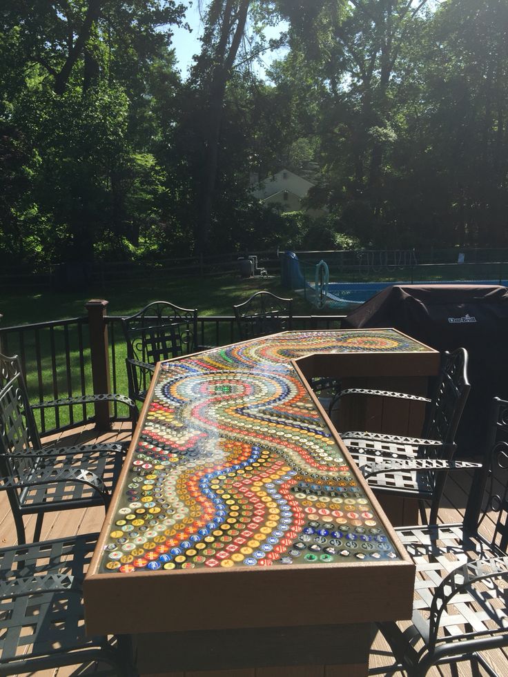 an outdoor table and chairs made out of beer bottle caps on a deck with a pool in the background