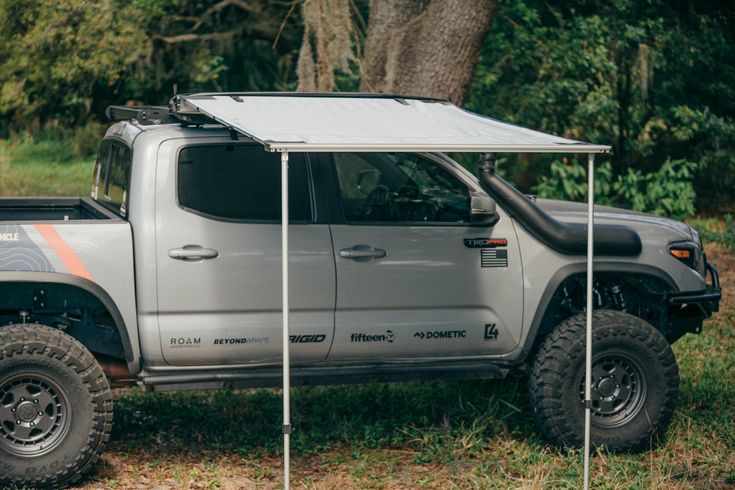 a truck with a tent attached to it parked in the grass next to some trees