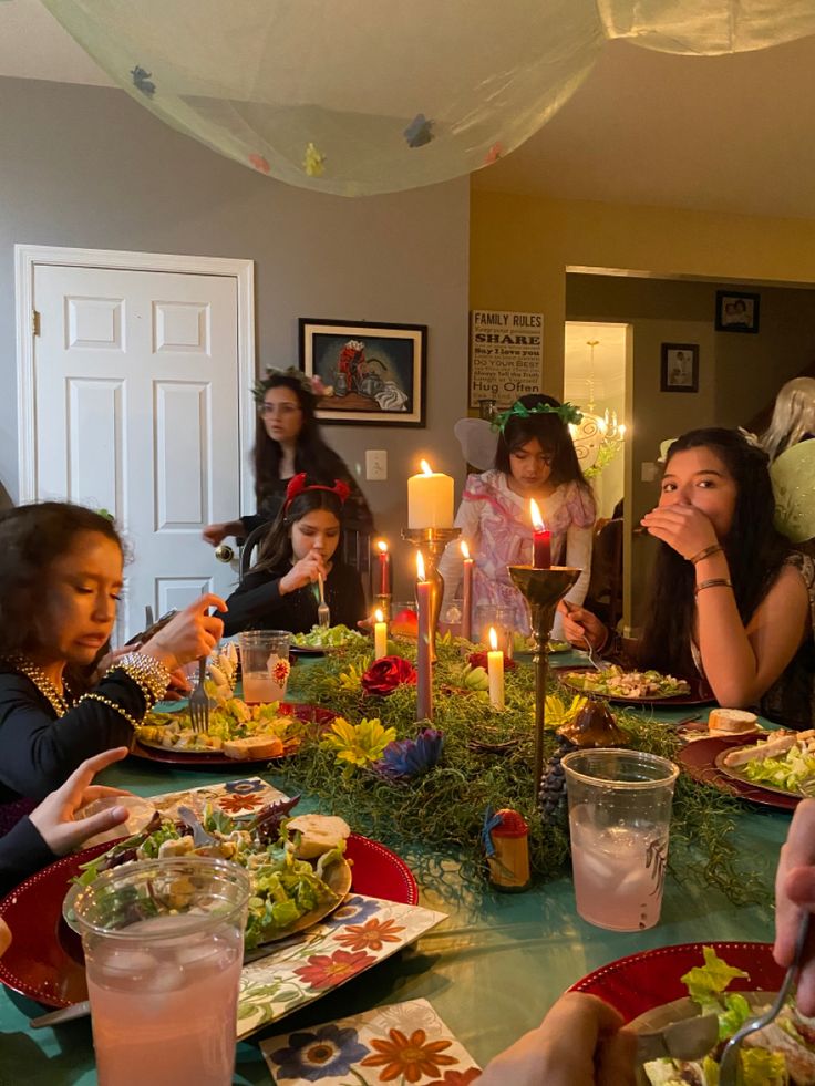 a group of people sitting around a table with plates of food and candles in front of them