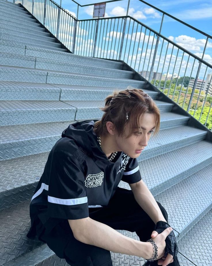 a young man sitting on the steps with his hands in his pockets and wearing a black hoodie