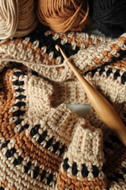 a crocheted blanket with yarn and a wooden knitting needle