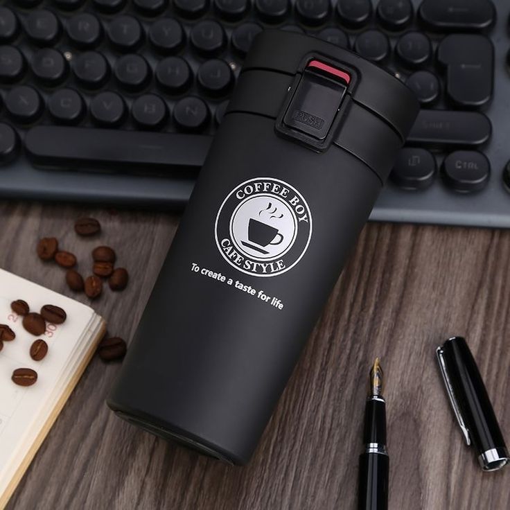 a coffee cup sitting on top of a wooden desk next to a keyboard and pen