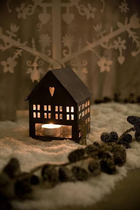 a small lit candle in the shape of a house on top of snow covered ground