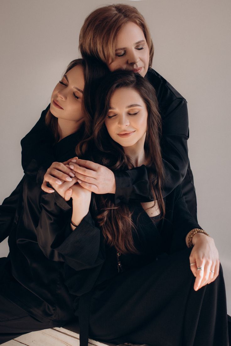 three women sitting on top of each other in black dresses and one is holding her arms around the other