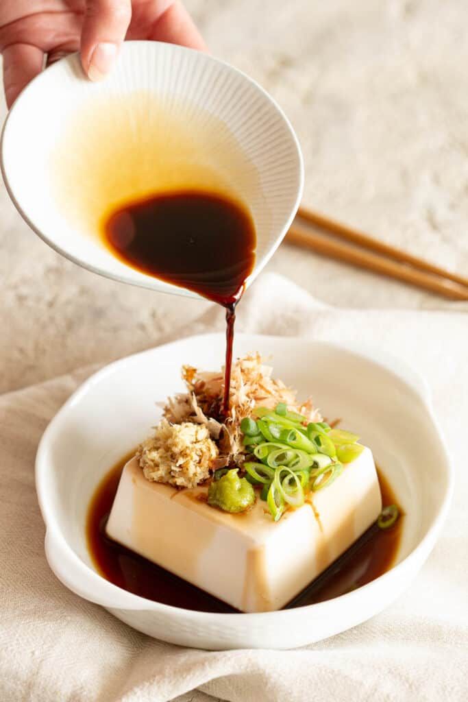 someone is pouring sauce on some food in a white bowl with chopsticks next to it