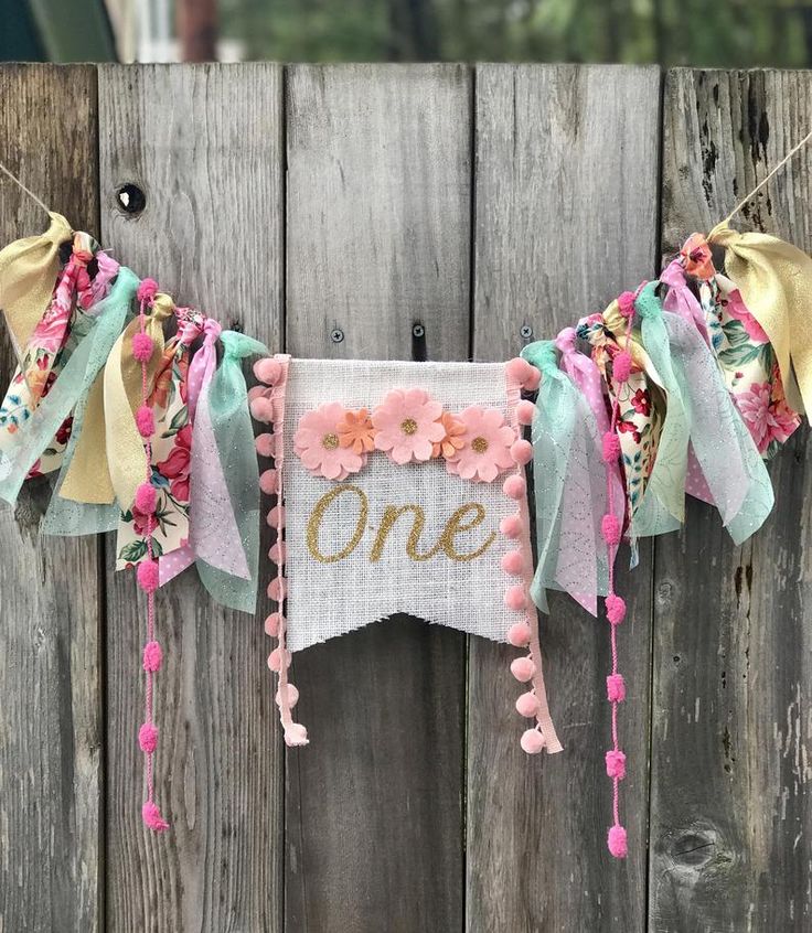 a one year old banner hanging on a fence with flowers and pom poms