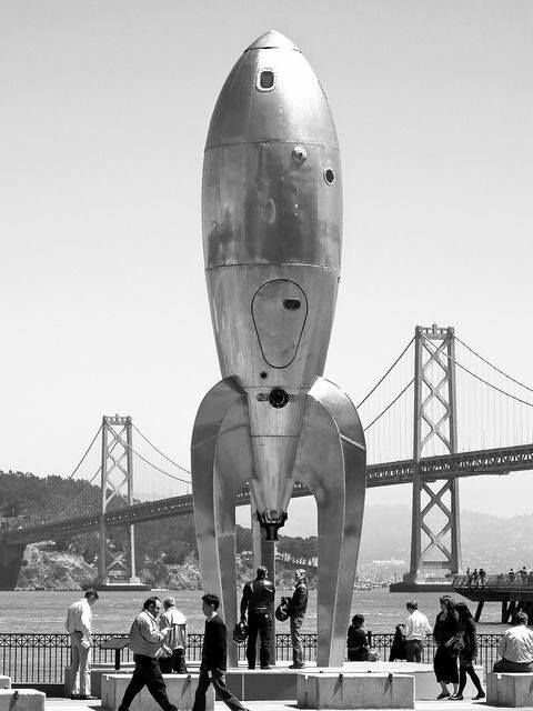 people are walking around in front of a large metal object with a rocket on it