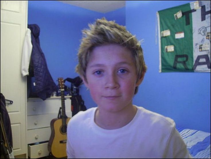 a young boy with blonde hair standing in front of a blue wall