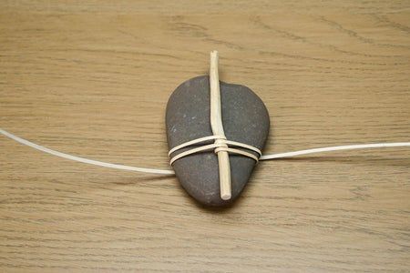 a rock with a cross on it is tied to a string and sits on a wooden surface