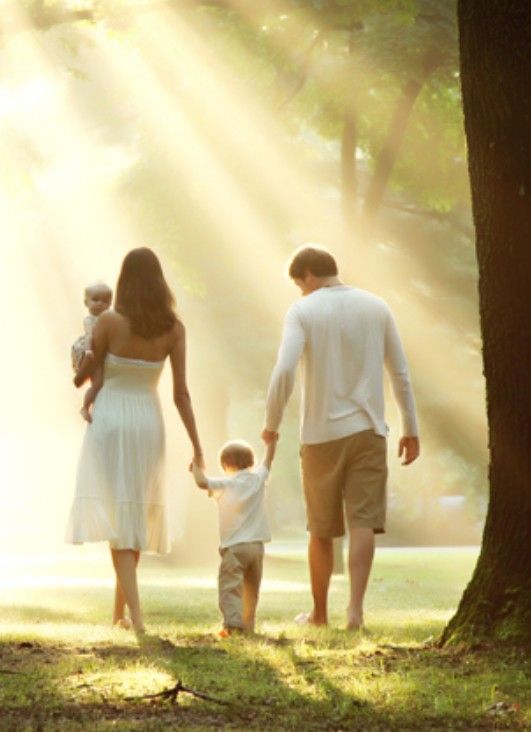 a man and woman holding hands while walking with their child in the park at sunset