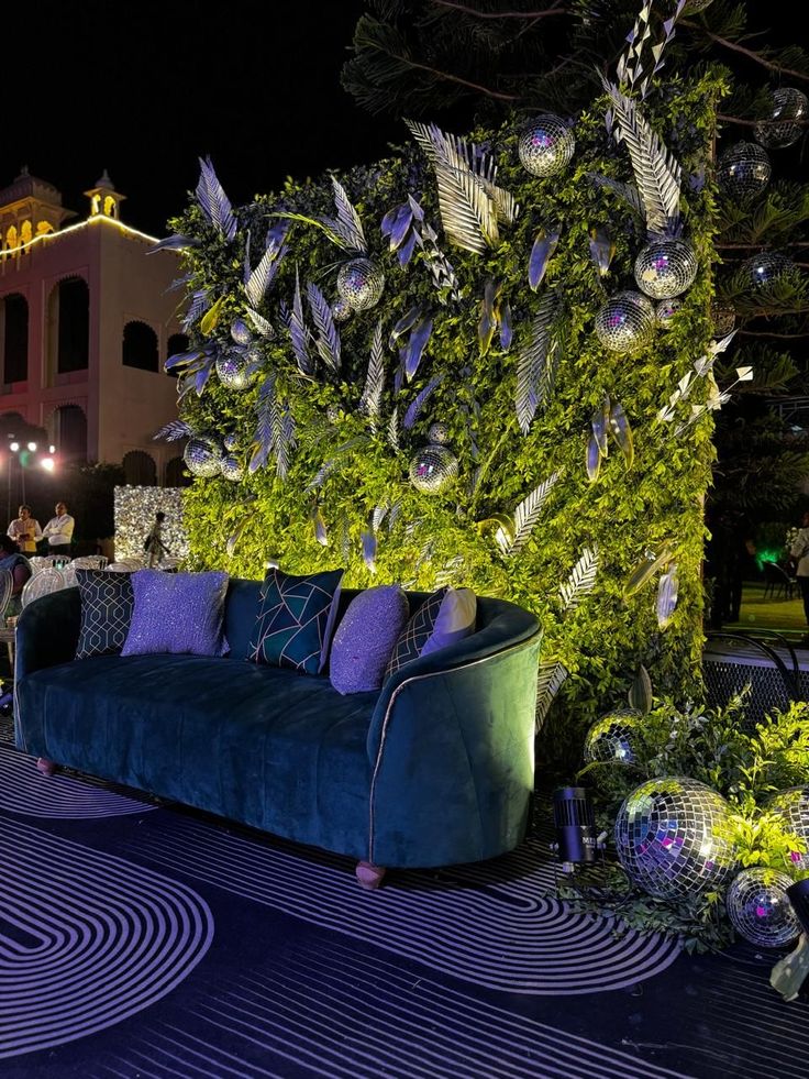 a couch sitting on top of a blue rug next to a lush green plant covered wall