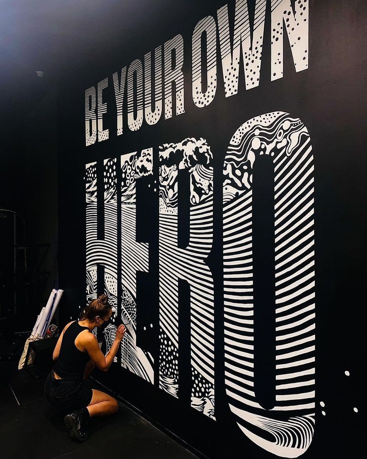 a woman sitting on the ground in front of a black and white sign that says be your own