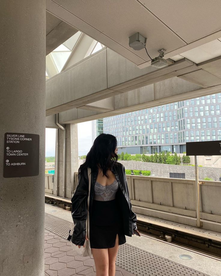 a woman is standing on the platform waiting for her train