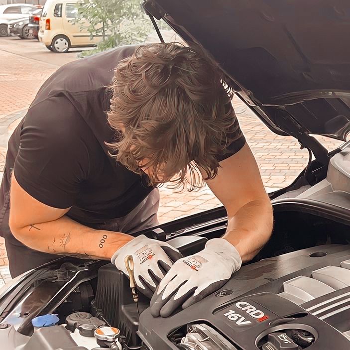 a man working on an engine in the hood of a car while wearing gloves and holding a wrench