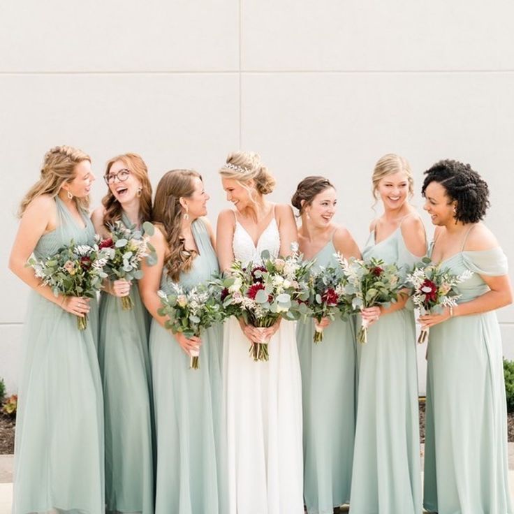 a group of women standing next to each other wearing dresses and holding bouquets in their hands