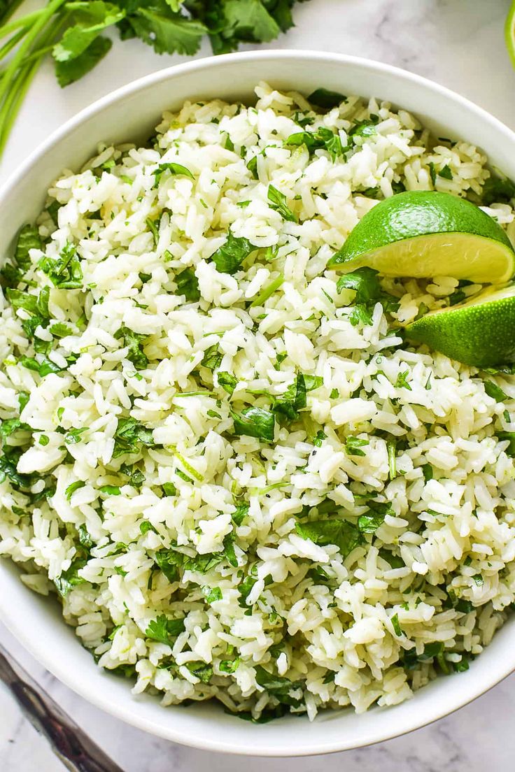 a white bowl filled with rice and garnished with cilantro next to limes