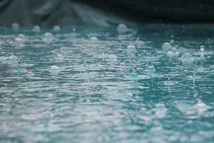 several drops of water floating on top of each other in a pool with rocks behind them