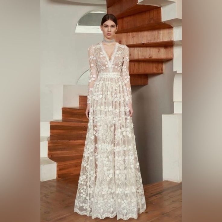 a woman standing in front of a staircase wearing a long white dress with flowers on it