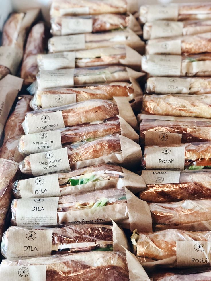 many sandwiches wrapped in brown paper are stacked on top of each other and labeled with labels