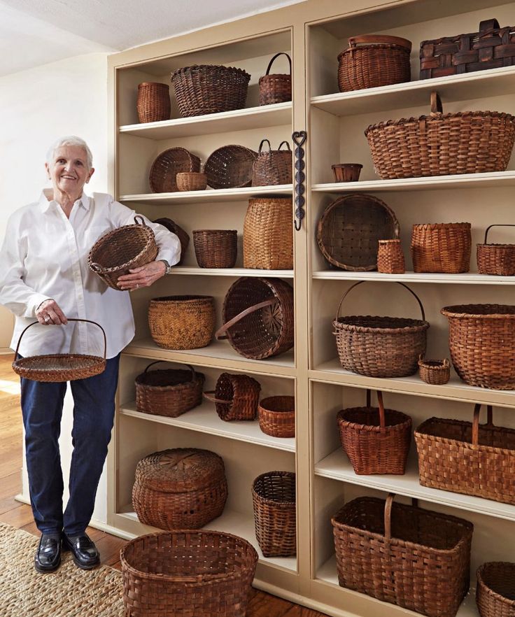 an older woman is standing in front of some baskets on shelves and holding a basket