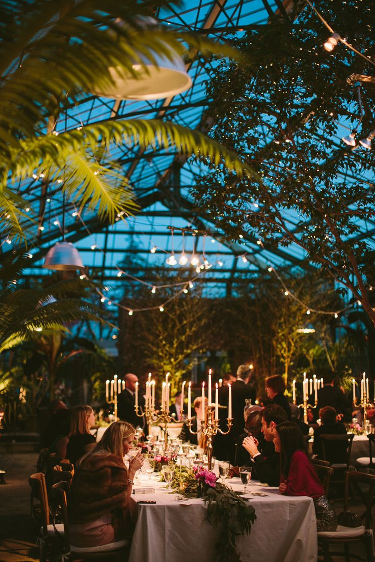 people sitting at tables with candles and flowers in front of the glass ceilinged room