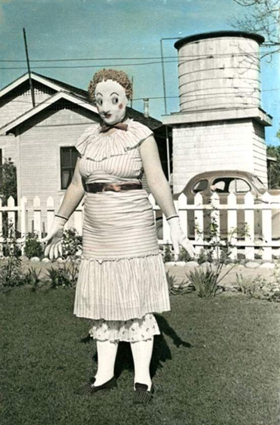 an old photo of a woman dressed as a clown in front of a farm house