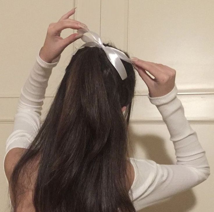 a woman with long hair is holding her head in one hand and wearing a bow on the other