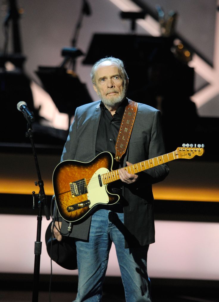 a man with a guitar standing in front of a microphone